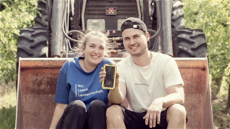 Anna und Johannes sitzen am Frontlader ihres Traktors und präsentieren die beste Outdoor-Handyhülle von 2022.