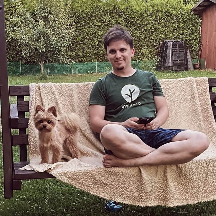 Georg Kanz, Gründer von Pinwald, sitzt mit seinem kleinen Hund auf einer Holzbank. Er hat braune Haare und trägt ein grünes Shirt mit dem Pinwald-Logo