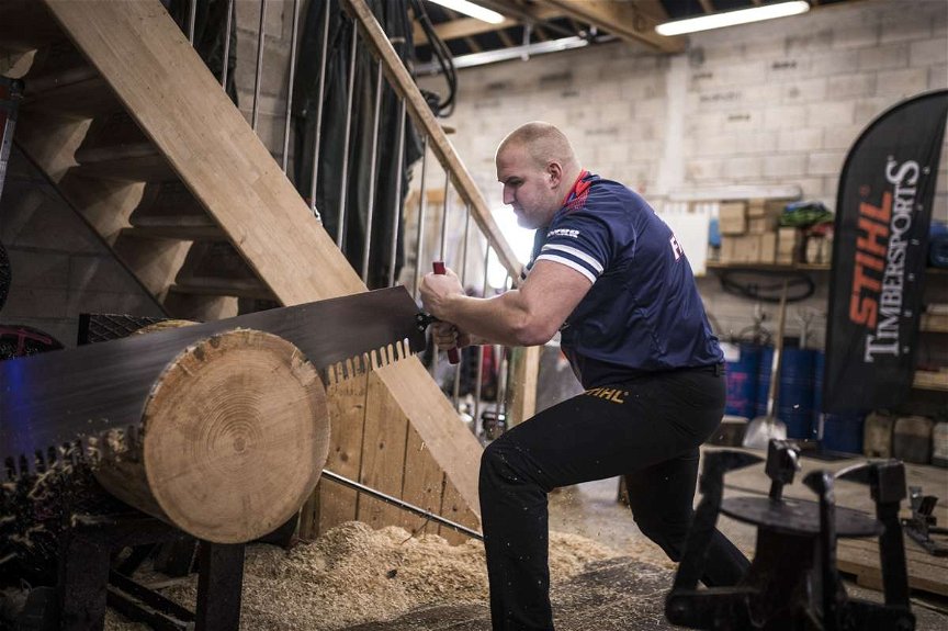 STIHL Timbersports Athlet schneidet in seiner Werkstatt mit einer Zugsäge eine Scheibe Holz von einem Baumstamm
