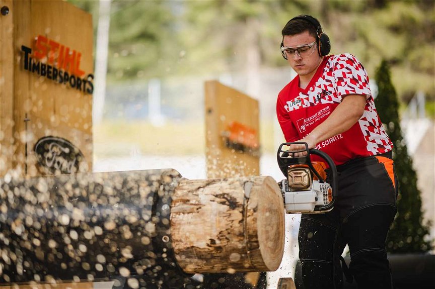 Junger STIHL Timbersports Athlet schneidet mit einer Motorsäge eine Scheibe von einem Holzstamm ab