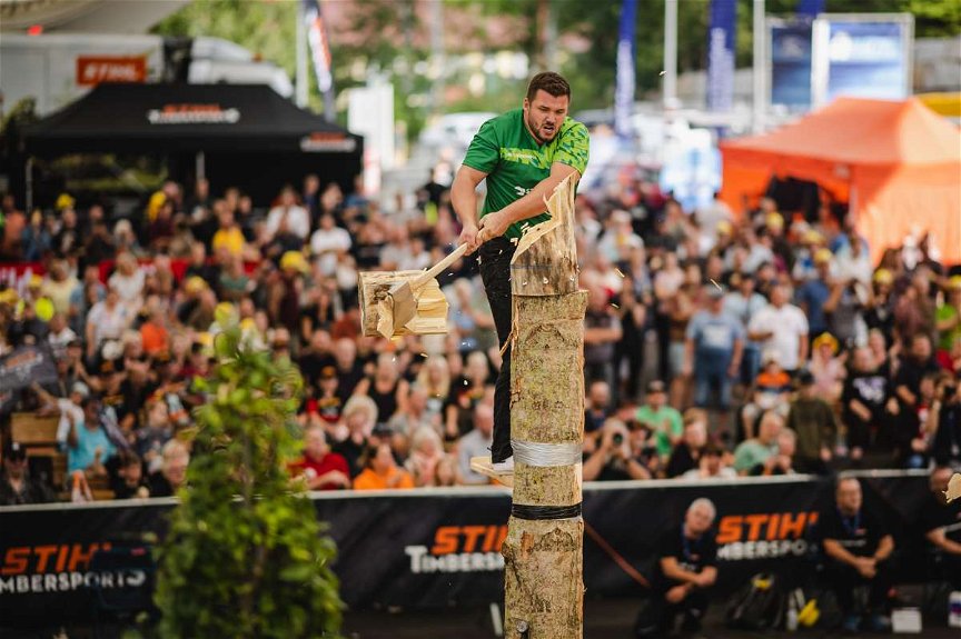 STIHL Timbersport Athlet steht auf einem Brett und zerhackt einen Baumstamm in mehreren Metern Höhe