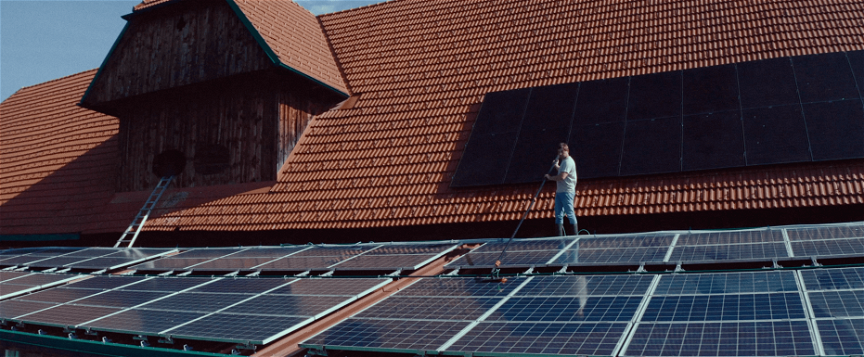 Landwirt Heribert steht auf dem Dach seines Stalls und reinigt seine Photovoltaikanlage.